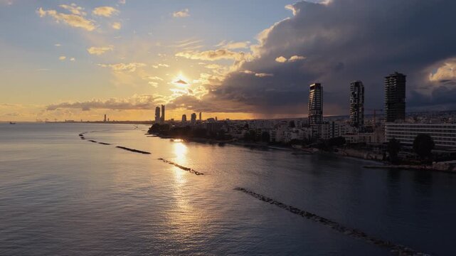 Aerial drone view of Limassol city coastline at sunset with warm golden light reflecting on the Mediterranean Sea