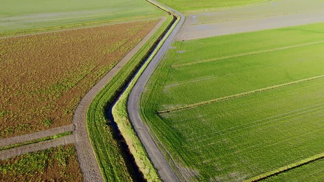 Aerial view of green agricultural fields and a narrow rural road with a drainage ditch in Mont Saint-Michel, Normandy, France.
