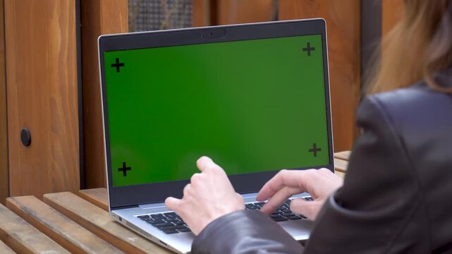 Woman typing on green screen laptop with tracking markers on a wooden table outdoors