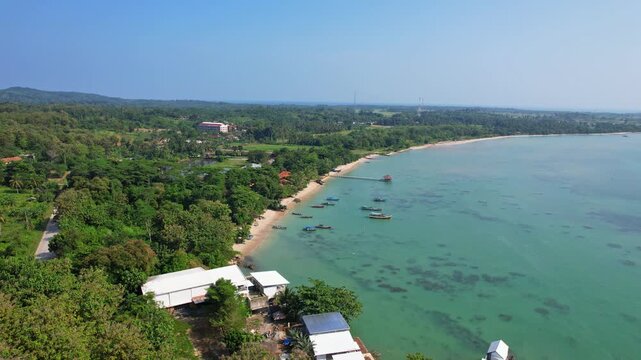 Aerial drone footage of Cipanon beach, a white sandy beach bay with small wooden fishing boats, village, in Pandeglang regency, Banten, Java island, Indonesia, with Tanjung Lesung tourism spot behind