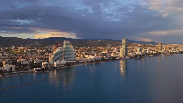 Aerial drone view of Limassol coastline showing modern architecture, residential buildings and calm Mediterranean waters under soft evening light