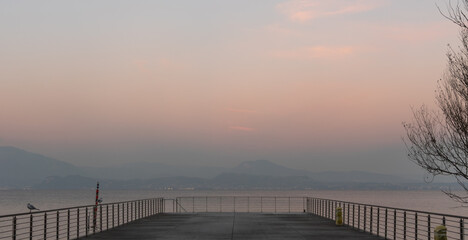Fototapeta premium Empty pier on Lake Garda at sunset with mountains and calm water, Italy