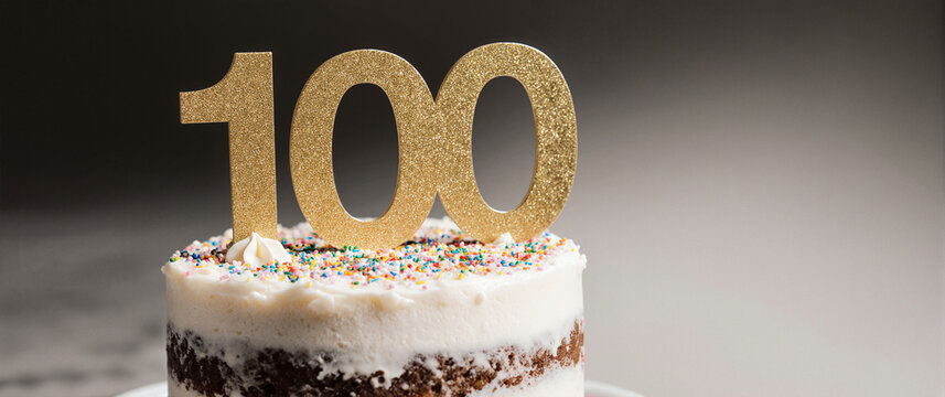 Elegant white celebration cake with golden 100 topper, milestone events