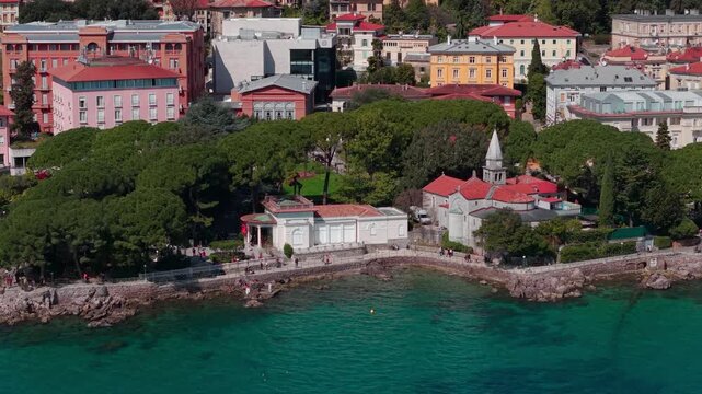 Aerial view of rocky coastline with small Church of St. James (Crkva sv. Jakov) and dense pine trees in Opatija, clear Adriatic water surrounding a scenic coastal walkway