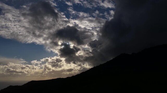 Aerial view of a dark mountain silhouette contrasting against a cloudy sky with patches of sunlight, creating a dramatic scene, Ponta Delgada, Sao Miguel, Portugal.
