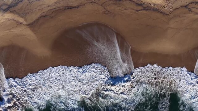 Aerial view of meeting point of the brown beach sand and the white foamy waves of the turquoise sea, Porto, Portugal.