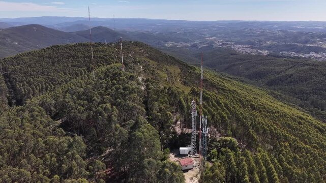 Aerial view of multiple antenna towers standing tall amidst a dense forest atop a mountain range, Valongo, Portugal.