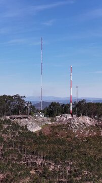 Aerial view of tall white and red radio towers standing on a hill in a forest under a clear blue sky, Valongo, Portugal.