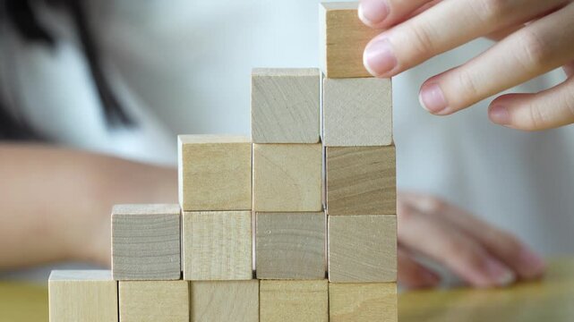 A child places the final wooden block on a rising staircase structure symbolizing steady growth, progress, and reaching new levels step by step.