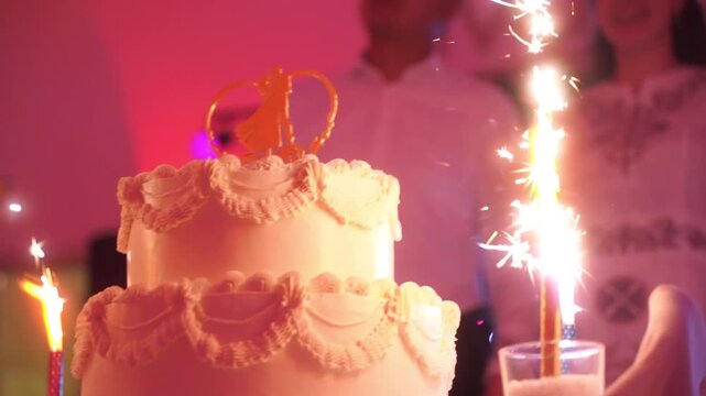 Elegant wedding cake with rings and white flowers, held by newlyweds in celebration