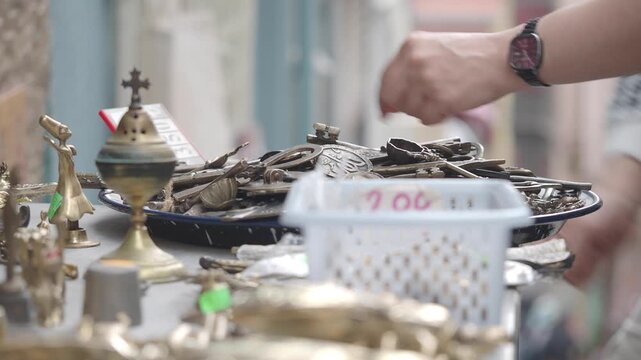 Woman picking through collection of vintage brass souvenirs at outdoor flea market counter.