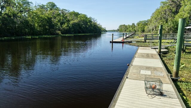 Aerial view of the dark river reflecting the sky, bordered by docks and lush green trees, creating a serene contrast, St. Augustine, Florida, United States.