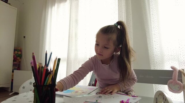 Cute little girl enjoys painting. Girl drawing and coloring picture with color pencil in her room at home