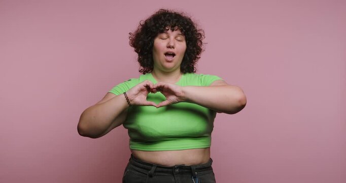 Woman makes heart shape with hands and smiles, then plays with hair and touches face in simple act of joy