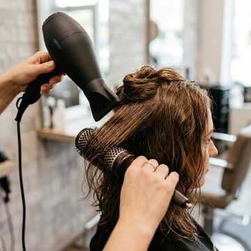 Close-up of a professional hair styling process showing a woman's hair being blow-dried with a round brush for volume and shine in a beauty salon