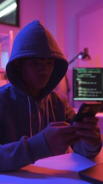 A mysterious hooded hacker using on a mobile phone in a dark room.