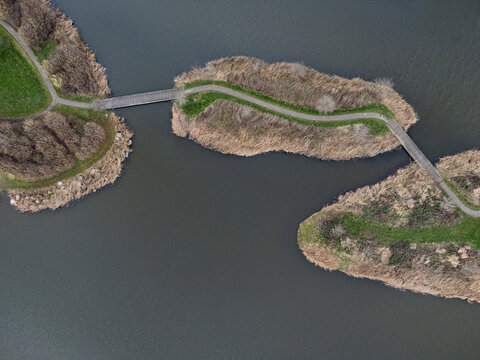 Aerial view of interconnected islands with winding paths, contrasting the muted browns of dormant vegetation with the cool blues of surrounding water, Overgooi, Flevoland, Netherlands.