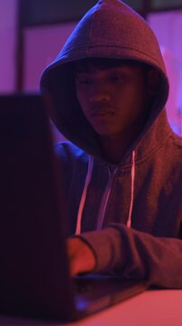 A mysterious hooded hacker working on a computer in a dark room.