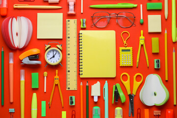 Different school stationery supplies with alarm clock and eyeglasses on red background