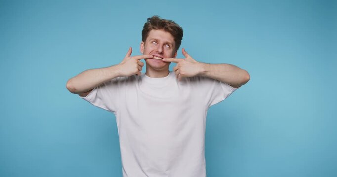 Man makes funny faces in front of blue background while posing with hands