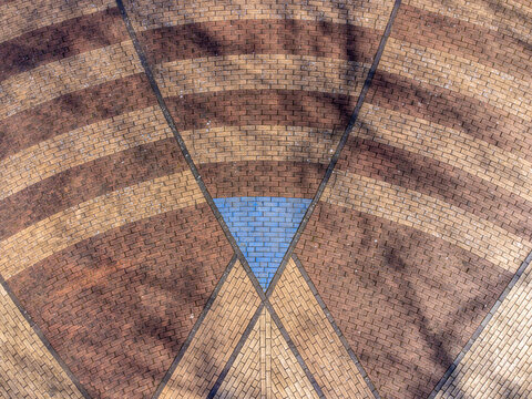 Aerial view of a patterned brick ground with contrasting brown and tan hues converging towards a central blue triangular accent, Maastrichtkwartier, Flevoland, Netherlands.