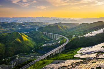 Aerial view of modern highway bridge and solar farm in mountain landscape at sunset. Renewable energy and infrastructure concept. © ABCDstock