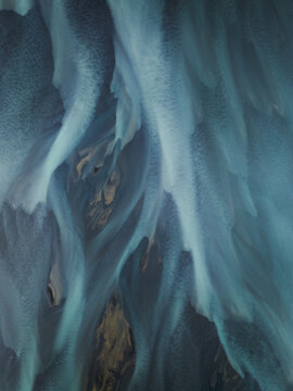 Aerial view of glacial rivers carve intricate patterns across the landscape, a symphony of blues and greys contrasting against the dark earth, Iceland.