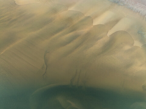 Aerial view of rhythmic patterns etched in the sand by the ocean's gentle caress, creating a mesmerizing mosaic of textures and tones, Iceland, Iceland.