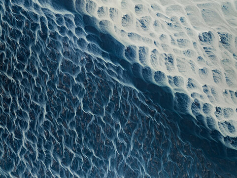 Aerial view of braided glacial rivers carving through stark, contrasting landscapes, a mesmerizing dance of dark waters against pale earth, Iceland.