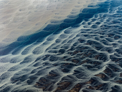 Aerial view of braided glacial rivers carve intricate patterns across the landscape, a dance of icy blues and earthy browns creating a mesmerizing natural artwork, Iceland, Iceland.