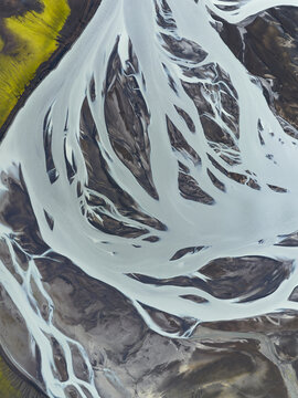 Aerial view of glacial rivers carving through the volcanic landscape, creating a mesmerizing dance of white against the dark earth, Highlands, Iceland.