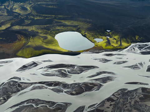 Aerial view of glacial rivers carving through volcanic ash and green moss, creating a stark contrast of textures and colors, Highlands, Iceland.
