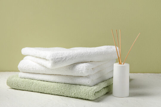 Stack of clean towels and reed diffuser on light table near color wall