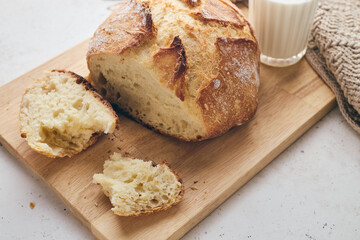 Sliced artisan sourdough bread with airy crumb on wooden board, glass of milk, and knitted cloth....