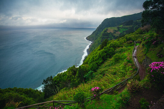 Aerial view of rugged cliffs draped in emerald vegetation meet the sapphire ocean under a moody sky, Ponta Delgada, Azores, Portugal.