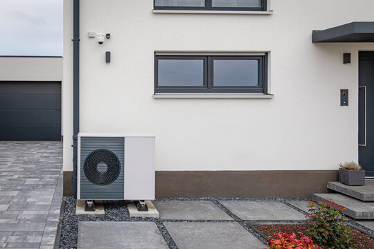 Modern air-to-water heat pump system installed outside a contemporary white family house for energy efficient heating