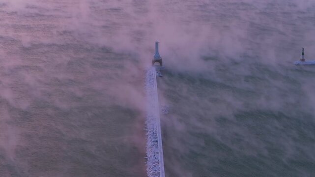 Cinematic winter morning: Bird's eye view of icy breakwater beacon in Sea Fog