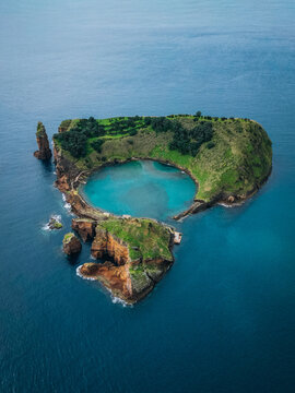 Aerial view of the lush green islet with a stunning turquoise crater lake contrasts sharply against the deep blue sea, Vila Franca do Campo, Portugal.