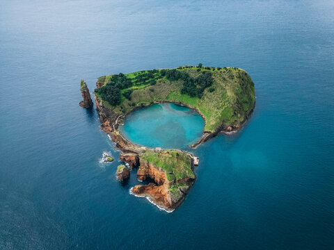 Aerial view of an islet with lush green vegetation and a serene blue lagoon surrounded by deep blue waters, Vila Franca do Campo, Azores, Portugal.