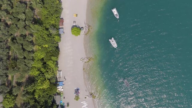 Top down shot of a beach at lake Garda near limone (Italy) 4K 60 fps slow motion possible , Summer time , clear water with boats