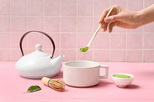 Female hand with chashaku and cup of tasty matcha tea on pink wooden background
