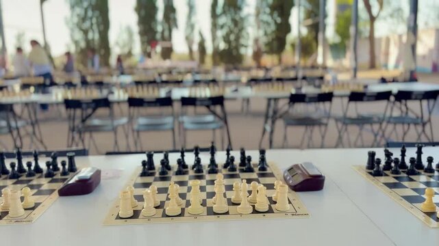 Chess boards with clocks at tournament hall, no people visible. Focus on game setup with blurred background of multiple tables, strategy and competition concept.