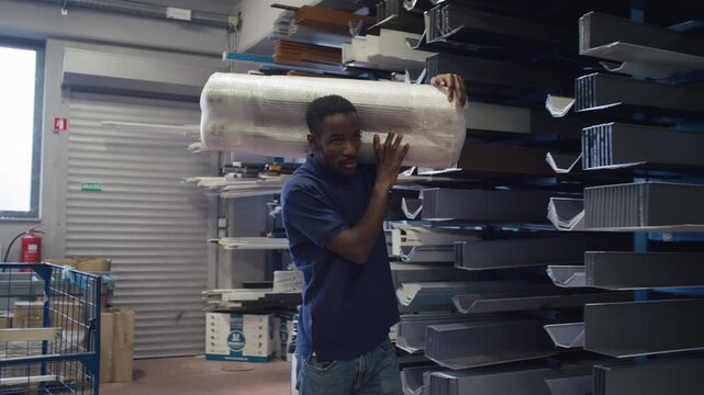 Warehouse worker manually handling heavy, packaged goods on his shoulder in logistics settings, having a physically demanding job.