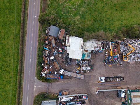Aerial view of a chaotic scene of scrap metal and machinery contrasts with the adjacent lush green fields and the stark grey road, Stafford, England, United Kingdom.