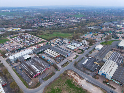 Aerial view of industrial buildings casting long shadows on the asphalt, juxtaposed against verdant fields and distant residential areas, Coventry, United Kingdom.