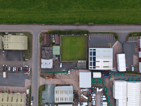 Aerial view of buildings and a green field intersected by roads, contrasting with the surrounding greenery, Tamworth, United Kingdom.