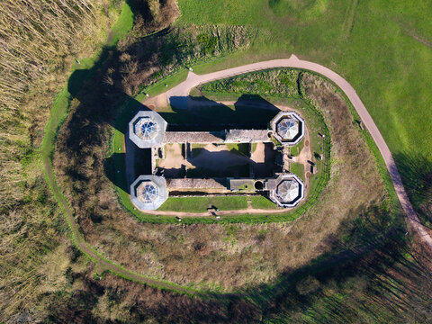 Aerial view of the stark, imposing fortress of Stafford Castle, its weathered stone walls contrasting with the vibrant green of the surrounding moat and parkland, Stafford, England, United Kingdom.