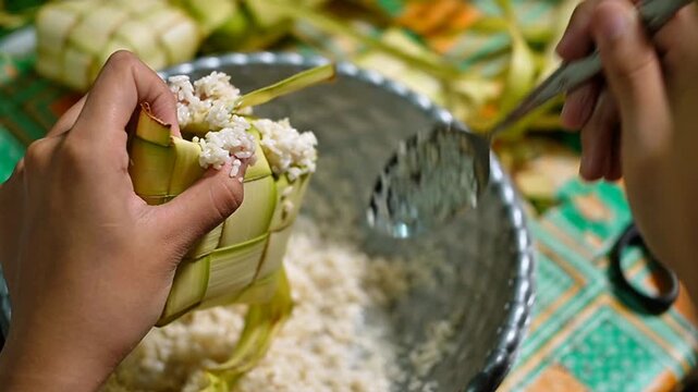 Authentic process of making ketupat rice cakes for Lebaran holiday, hand putting raw rice into diamond-shaped woven palm leaves, Islamic religious festival traditions, Southeast Asian cuisine