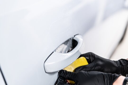 Close-up of a detailer applying paint protection film (PPF) around a car door handle. This area is highly prone to scratches, and the film provides durable protection against daily wear.
