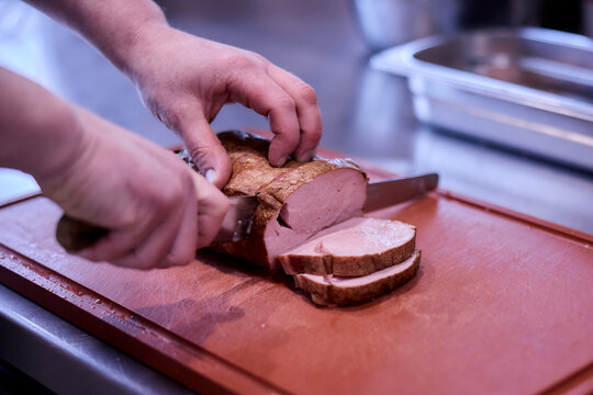 Koch schneidet saftigen Braten oder Leberk&auml;se in Scheiben.